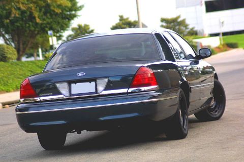 1998 Ford Crown Victoria - dark blue Ford Crown Victoria sedan with black wheels shot from the rear left three-quarter on a road, with motion blur.