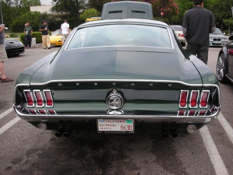 1998 Ford Crown Victoria - rear of a dark green Mustang fastback shows its taillights and a California historical-vehicle license plate at a car meet.