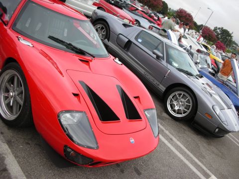 1998 Ford Crown Victoria - red Ford GT-style supercar and a silver Ford GT with racing stripes sit side by side among rows of cars at an outdoor meet.