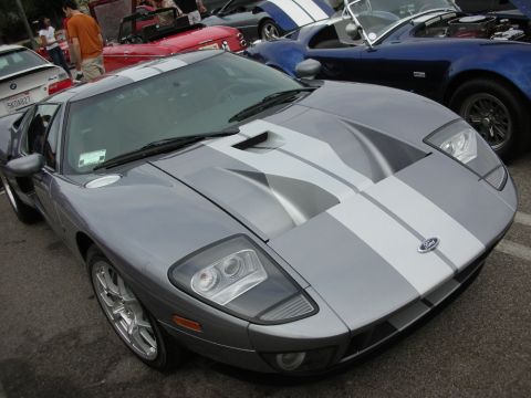 1998 Ford Crown Victoria - silver Ford GT with twin white racing stripes is parked near a blue Dodge Viper and other cars on a sunny lot.