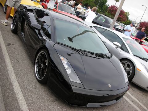 1998 Ford Crown Victoria - black Lamborghini Gallardo coupe with dark wheels sits low among other supercars on a crowded show lot.
