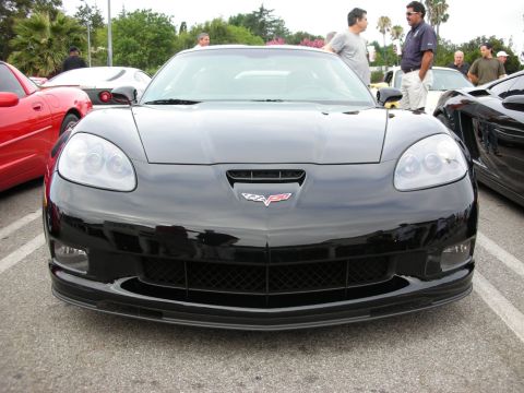 1998 Ford Crown Victoria - black front end of a Chevrolet Corvette shows its crossed-flags emblem and lower splitter, parked among other cars at a meet.
