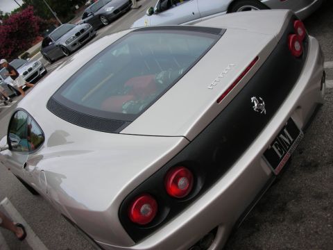 1998 Ford Crown Victoria - rear three-quarter of a silver Ferrari coupe shows round taillights, a prancing-horse badge, and a red interior in a parking lot.