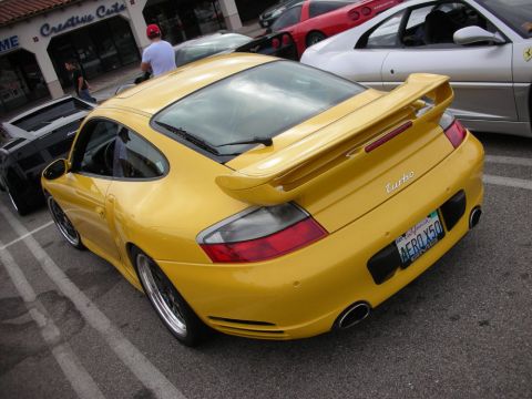1998 Ford Crown Victoria - yellow Porsche 911 Turbo with a large rear wing and dark wheels is parked among other cars on a sunny show lot.