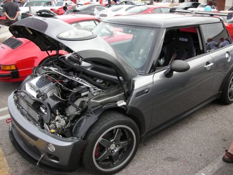 1998 Ford Crown Victoria - gray Mini Cooper hatchback sits with its hood open exposing the engine, parked beside red sports cars at a car meet.