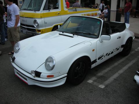 1998 Ford Crown Victoria - white classic Porsche 911 cabriolet with black Carrera script and black wheels is parked near a yellow Dodge van at a meet.