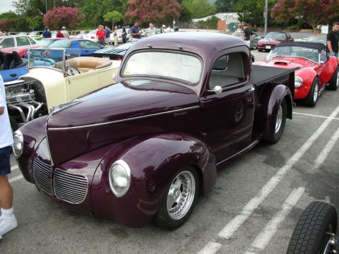 1998 Ford Crown Victoria - deep-purple vintage-style hot rod pickup with chrome wheels and a chopped cab sits among classic cars at an outdoor show.