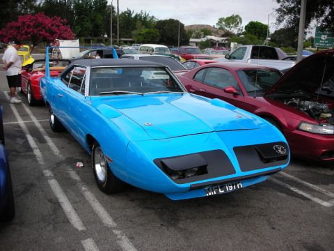 1998 Ford Crown Victoria - bright blue winged muscle car with a black vinyl top and tall rear wing sits parked among other cars at an outdoor meet.