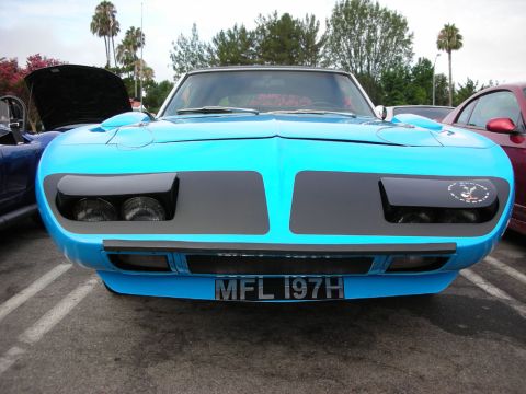 1998 Ford Crown Victoria - front of a bright blue winged muscle car shows its pointed nose cone, hidden headlights, and a MFL 197H plate among palm trees.