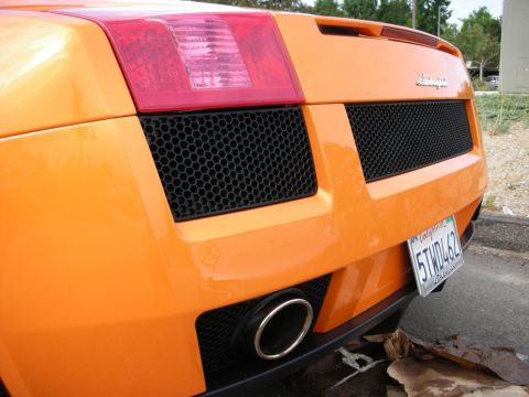 1998 Ford Crown Victoria - rear of an orange Lamborghini Gallardo shows its mesh grilles, taillight and a single exhaust tip with a California plate.