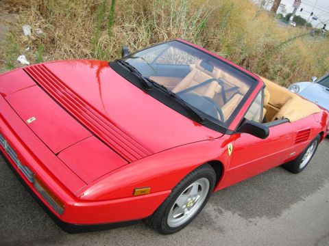 1998 Ford Crown Victoria - red Ferrari convertible sits top-down with its tan leather interior exposed, parked beside dry roadside brush.