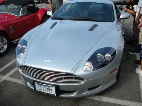 1998 Ford Crown Victoria - silver Aston Martin coupe shows its wide mesh grille and winged badge, with a red convertible behind it.