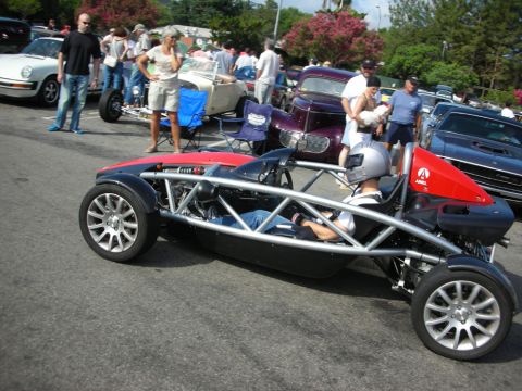 1998 Ford Crown Victoria - skeletal tube-frame Ariel Atom sports car sits among classic cars and onlookers at an outdoor gathering.