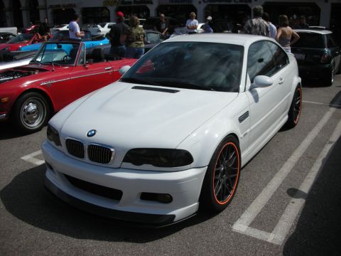 1998 Ford Crown Victoria - white BMW M3 coupe with orange-accented black wheels sits in a parking lot lined with other show cars.