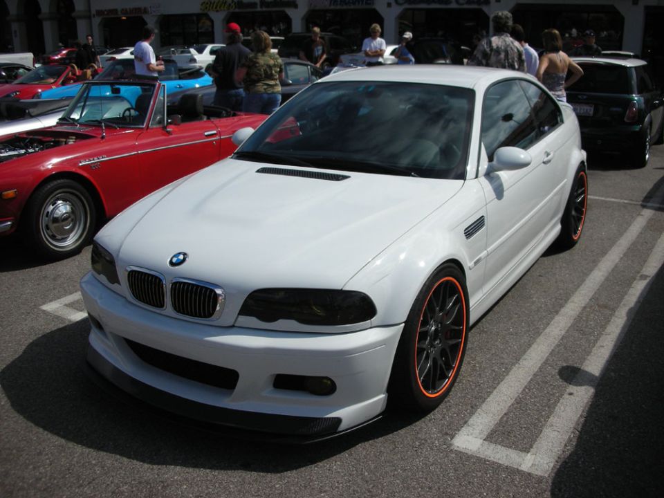 White BMW M3 coupe with orange-lipped black wheels at an outdoor car show
