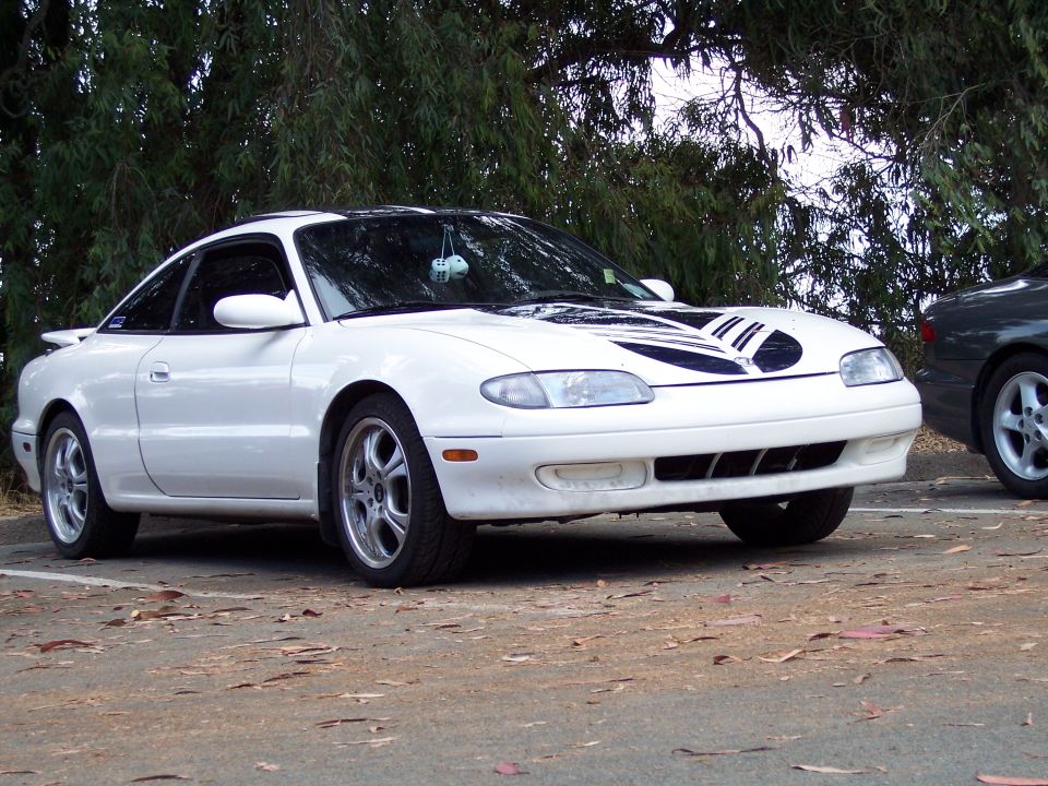 White Mazda MX-6 with black racing stripes on the hood parked outside