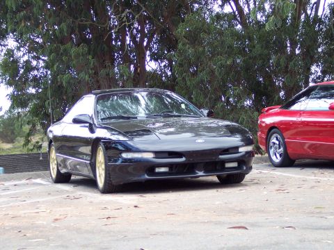 1995 Ford Probe - Two Ford Probes, one black and one red, are parked outdoors under trees.