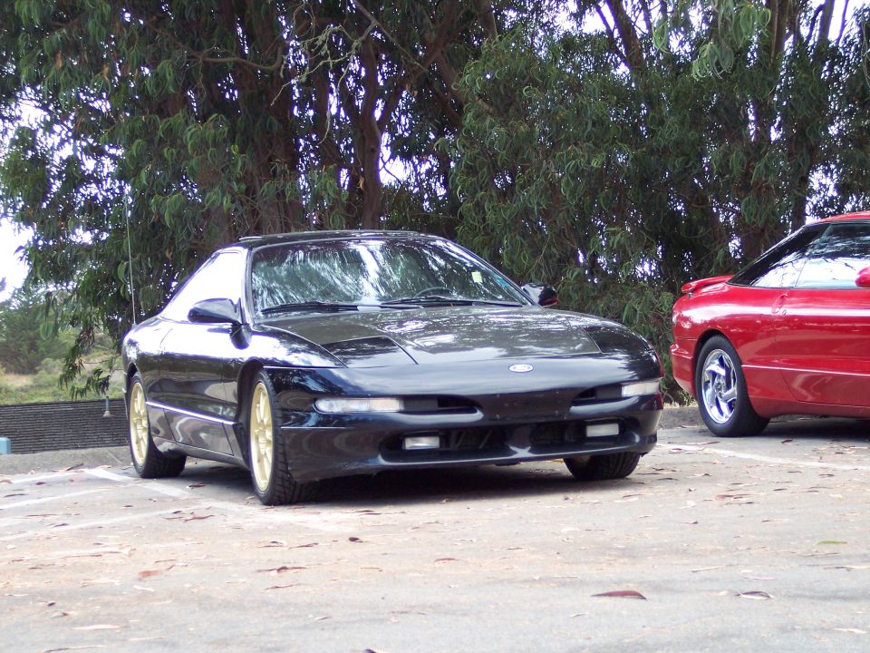 Black Ford Probe with gold wheels parked next to a red Ford Probe