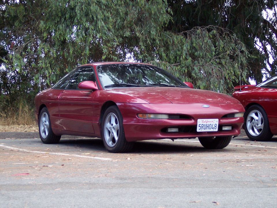 Red Ford Probe coupe parked under trees, front three-quarter view