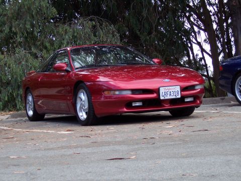 1995 Ford Probe - A red 1995 Ford Probe is parked outdoors, with trees in the background and another vehicle to its right.
