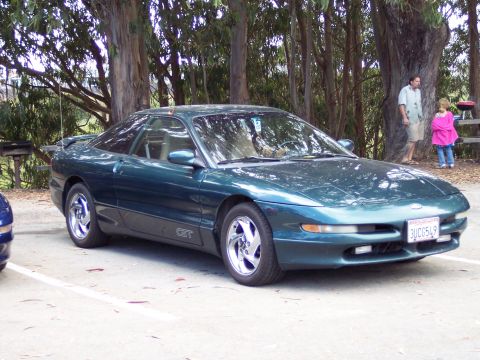 1995 Ford Probe - A teal 1995 Ford Probe GT coupe is parked outdoors near trees, with people in the background.