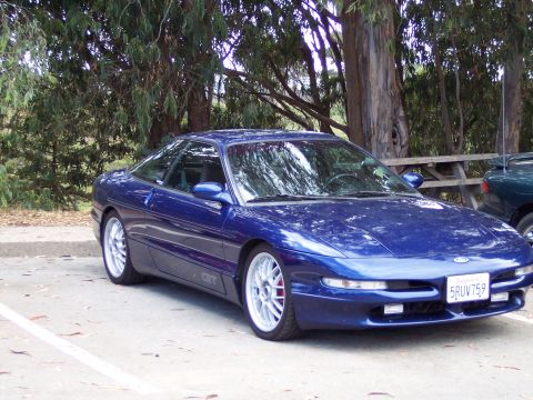 1995 Ford Probe - A blue Ford Probe is parked in a lot with trees and a picnic table in the background.