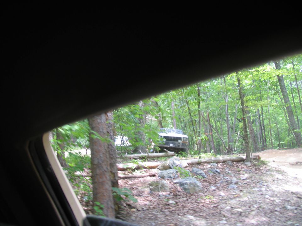 White truck parked on a dirt path in a forest, viewed from inside another vehicle