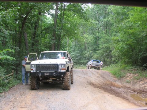 1995 Ford C-350 (Centurion Conversions) - A lifted 1978 Ford Bronco is parked on a dirt road with another truck in the background.
