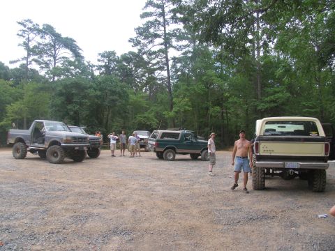 1995 Ford C-350 (Centurion Conversions) - A group of off-road vehicles and people gathered in a wooded area.