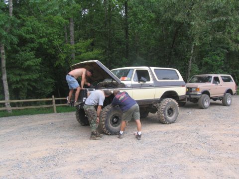 1995 Ford C-350 (Centurion Conversions) - Three men work on the hood of a lifted Ford Bronco, with another Bronco parked behind it.