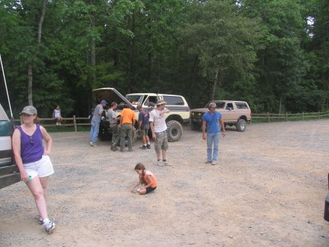 1995 Ford C-350 (Centurion Conversions) - Several people are gathered around a tan Ford Bronco with its hood open in a gravel lot.