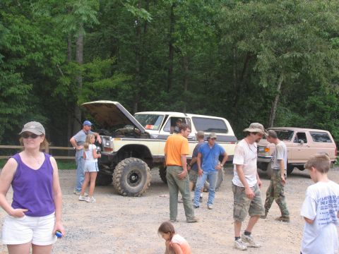 1995 Ford C-350 (Centurion Conversions) - A group of people stand around a lifted Ford Bronco with its hood up, with another SUV in the background.