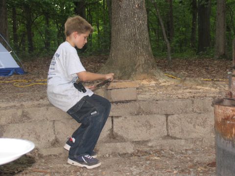1995 Ford C-350 (Centurion Conversions) - A young boy is focused on building with bricks while sitting on a stone wall in a wooded area.