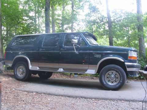 1995 Ford C-350 (Centurion Conversions) - Side view of a dark green 1995 Ford C-350 SUV with tan lower body trim, parked outdoors.