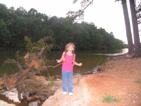 1995 Ford C-350 (Centurion Conversions) - A young girl with braided hair smiles by the water's edge, with a fallen tree nearby.