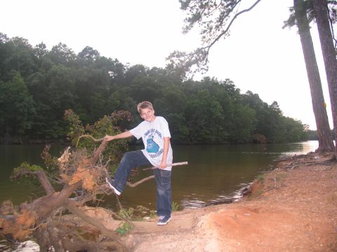 1995 Ford C-350 (Centurion Conversions) - Boy poses on a fallen tree by a lake with a wooded shoreline.