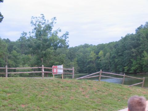 1995 Ford C-350 (Centurion Conversions) - A split-rail fence borders a grassy area leading to a lake, with a sign posted near the fence.