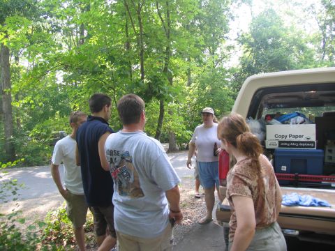 1995 Ford C-350 (Centurion Conversions) - People are gathered around the open tailgate of a tan pickup truck in a wooded area.