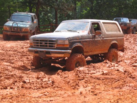 1995 Ford C-350 (Centurion Conversions) - Multiple off-road vehicles navigate a muddy terrain, with one Ford Bronco deeply mired.