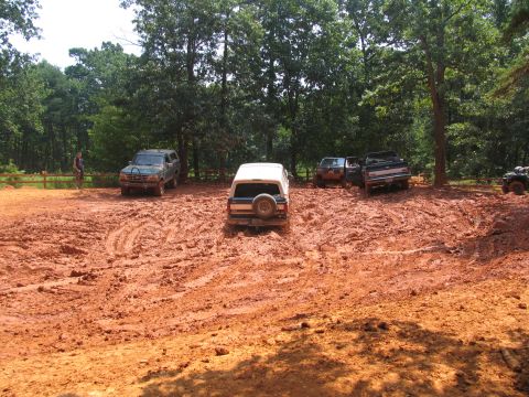 1995 Ford C-350 (Centurion Conversions) - Multiple off-road vehicles navigate a challenging muddy terrain during an outdoor event.