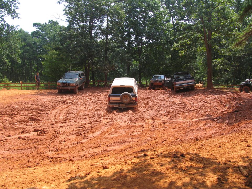 Several off-road vehicles stuck in thick red mud with trees in the background