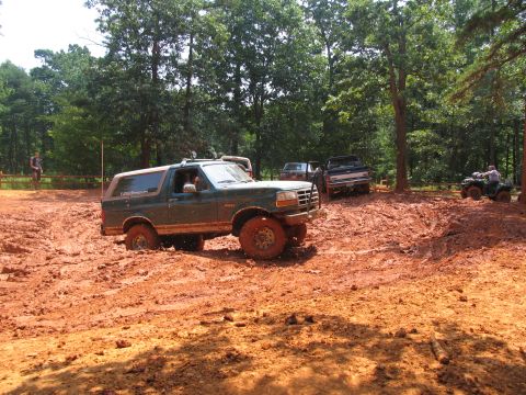 1995 Ford C-350 (Centurion Conversions) - A green Ford Bronco navigates a muddy off-road course, with other vehicles and an ATV visible in the background.