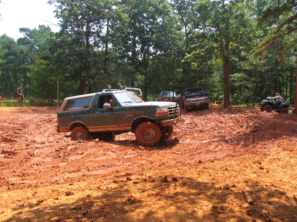 Green Ford Bronco stuck in mud, with other vehicles in the background