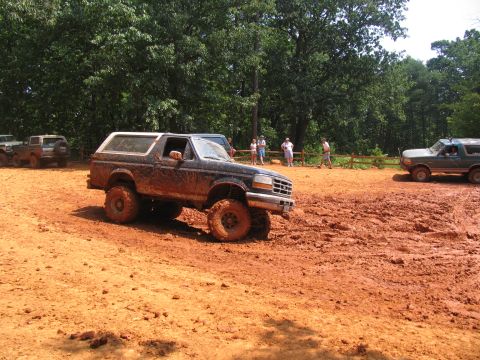 1995 Ford C-350 (Centurion Conversions) - Several vehicles are seen off-roading in a muddy area with trees in the background.