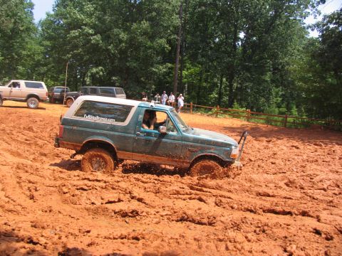 1995 Ford C-350 (Centurion Conversions) - A green SUV navigates a challenging mud pit, with other vehicles and spectators in the background.