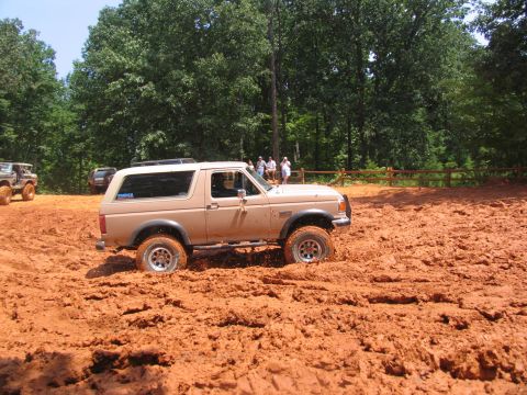 1995 Ford C-350 (Centurion Conversions) - A tan Ford Bronco navigates a muddy terrain, with spectators observing from a distance.