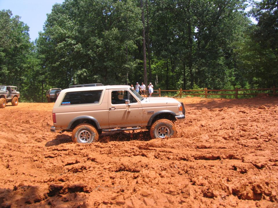 Tan Ford Bronco driving through mud, with people watching in the background