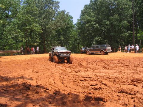 1995 Ford C-350 (Centurion Conversions) - Several off-road vehicles are navigating a muddy terrain with spectators observing from a distance.