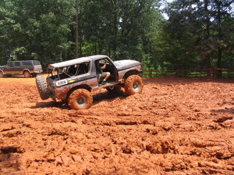 1995 Ford C-350 (Centurion Conversions) - A heavily modified Ford Bronco navigates a muddy off-road course, with another SUV visible in the background.
