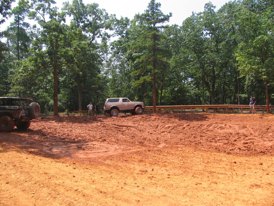 Tan Ford Bronco parked in mud with a spare tire on the back. Another vehicle is partially visible on the left
